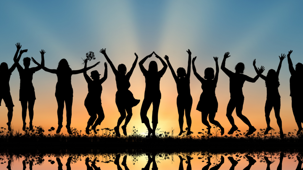 People jumping happily are silhouetted against the backdrop of a sunrise or sunset.