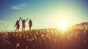 3 people crest a hill as the sun rises on the horizon.