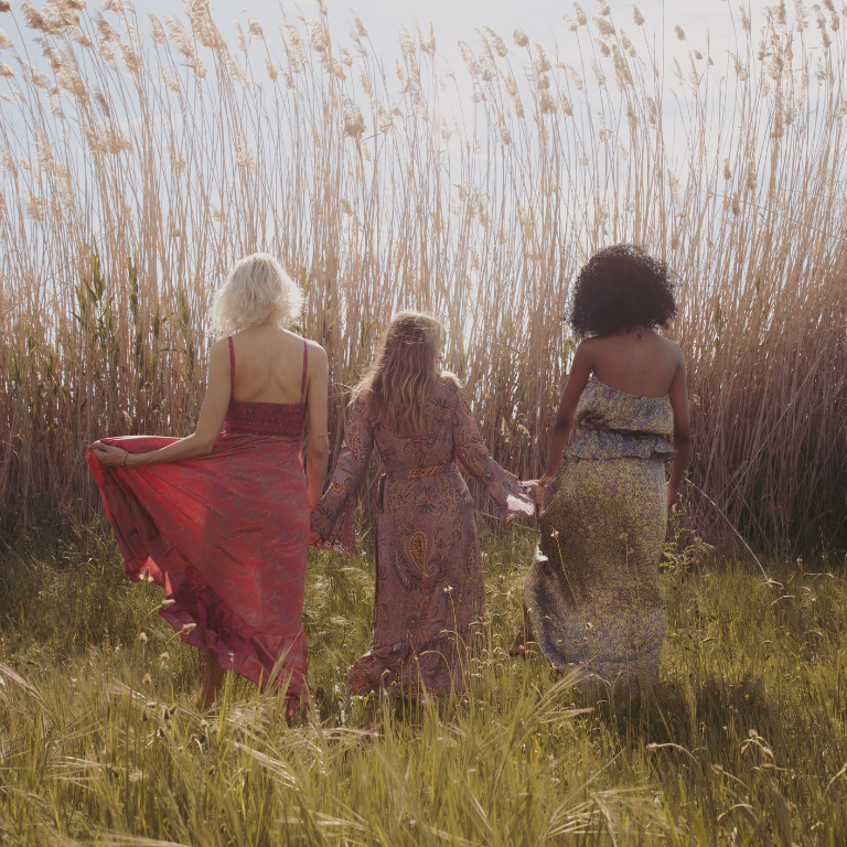 12 3 women hold hands as they walk into a tall field of wheat.