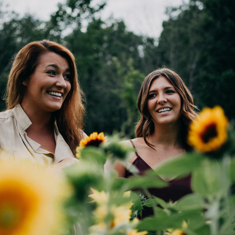 14 2 women stand in a cluster of sunflowers.