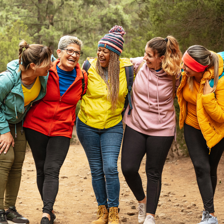 5 5 women in brightly colored hiking gear smile on a forest trail.