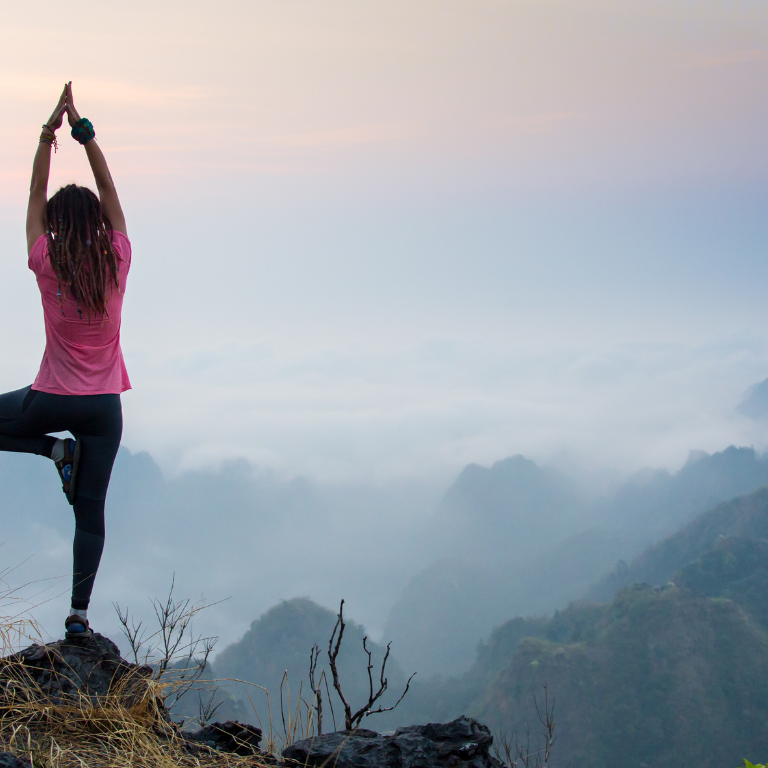 7 A woman strikes a yoga pose on top of a rock overlooking a mountain range.