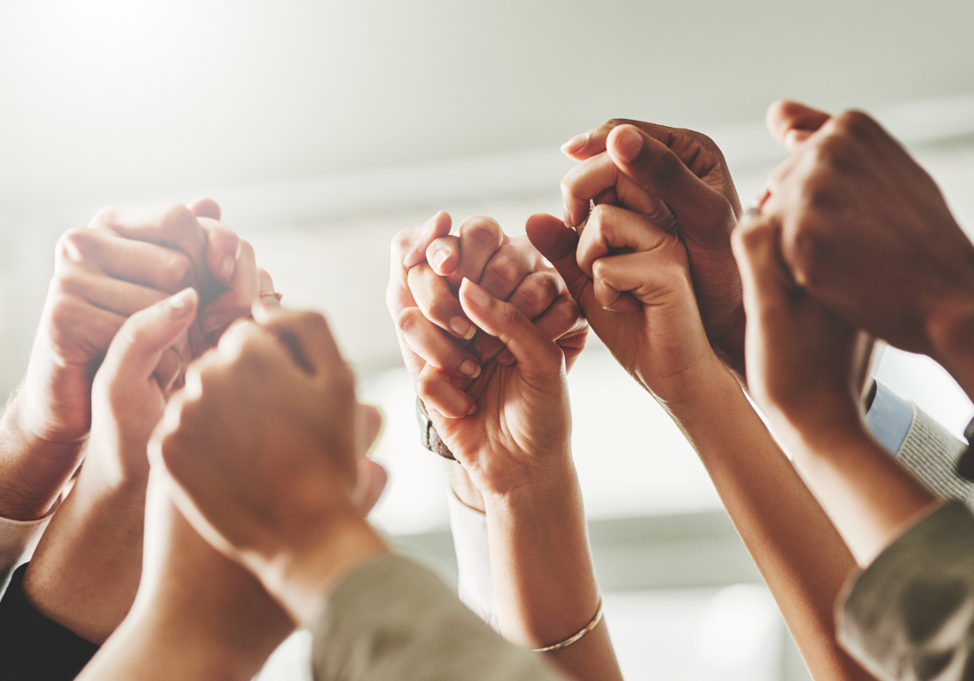 About Us People's hands clasped together and raised in the air.