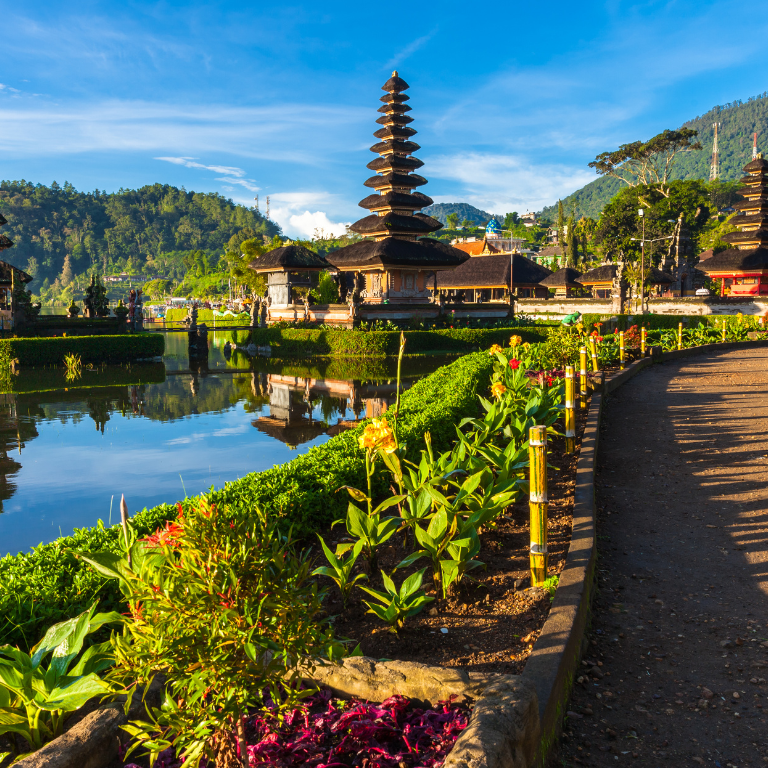 Picture of a walkway in Bali, with a large lake to the left and a temple ahead.