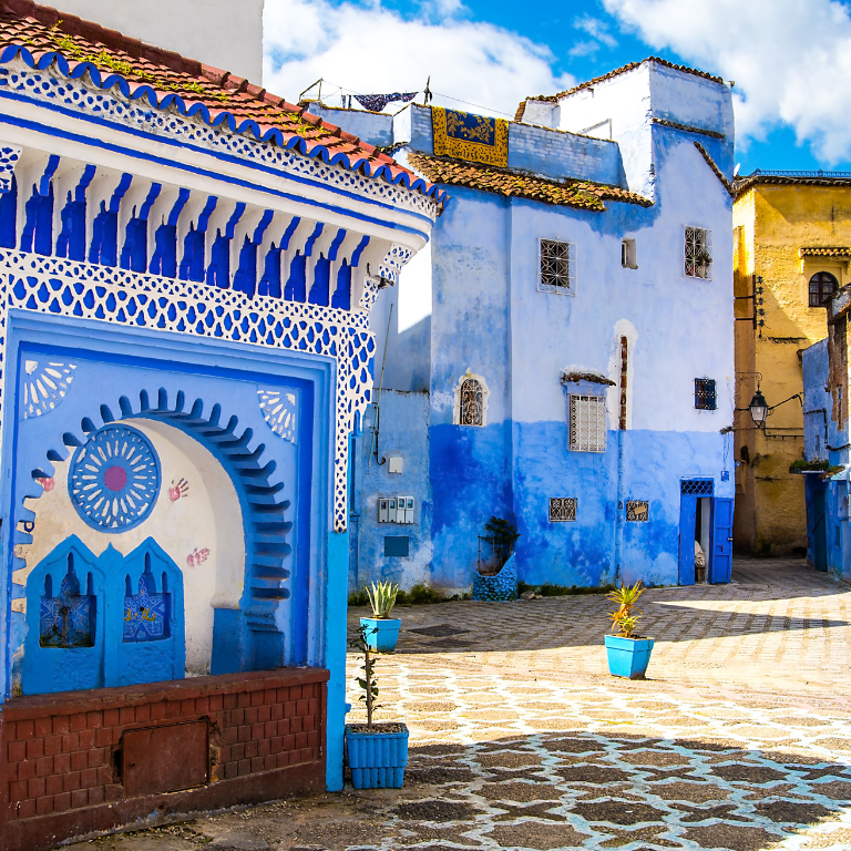 Enchanting blue-washed streets of Chefchaouen, Morocco, famously known as the Blue City, image features a beautifully adorned public fountain with intricate Moorish tilework and bold geometric patterns in shades of cobalt, azure, and white.