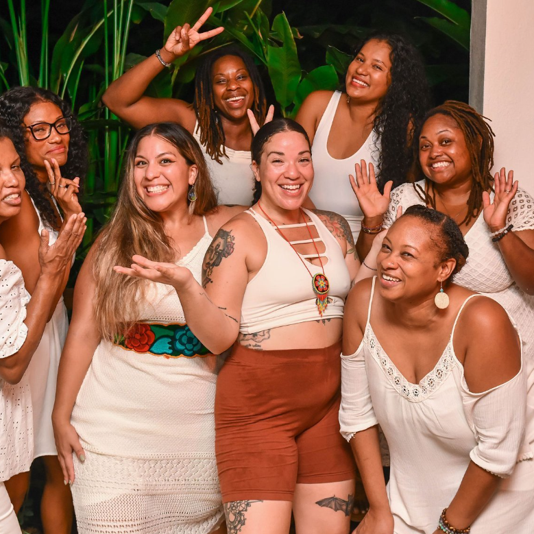 A diverse group of smiling women dressed mostly in white poses for a group photo.